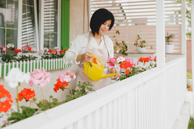 Mujer con cabello oscuro regando plantas en macetas geranios al aire libre