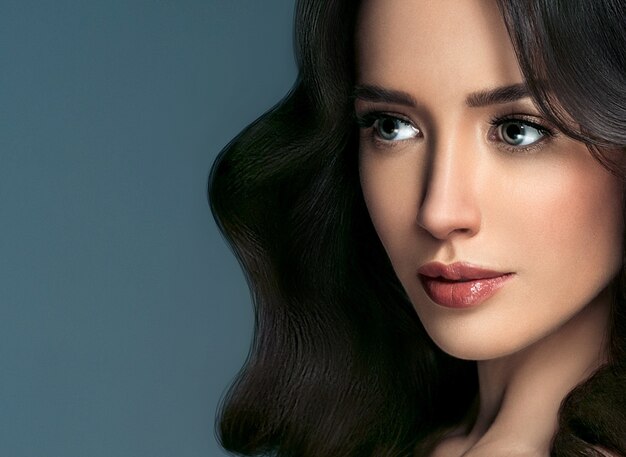 Mujer de cabello perfecto retrato femenino hermoso sobre fondo azul. Concepto de belleza de peinado largo y rizado de cuidado del cabello morena. Tiro del estudio.