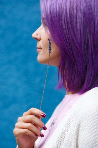 Mujer con cabello púrpura y colorido, gire su perfil con tallo de lavanda en la mano