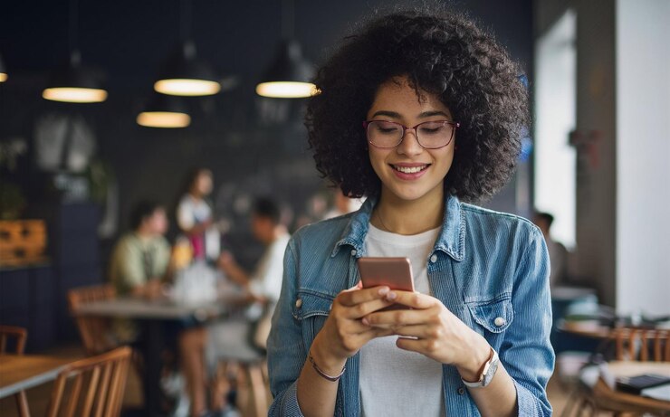 una mujer con cabello rizado está mirando su teléfono y sonriendo