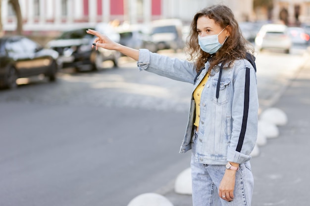 Foto mujer de cabello rizado con mascarilla atrapa auto en la ciudad en un día soleado