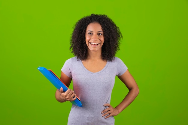 Una mujer con cabello rizado sostiene una libreta azul y sonríe.