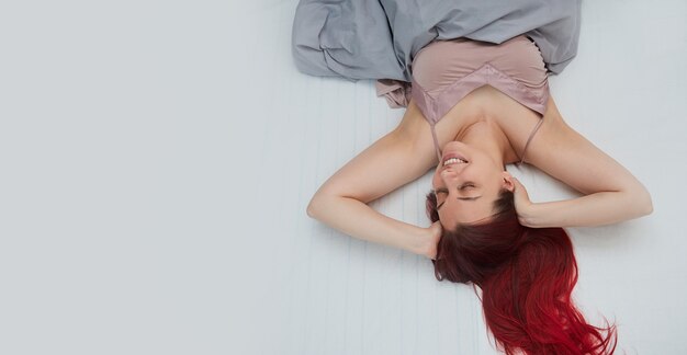 Mujer con cabello rojo se despierta sonriendo en la cama se estira