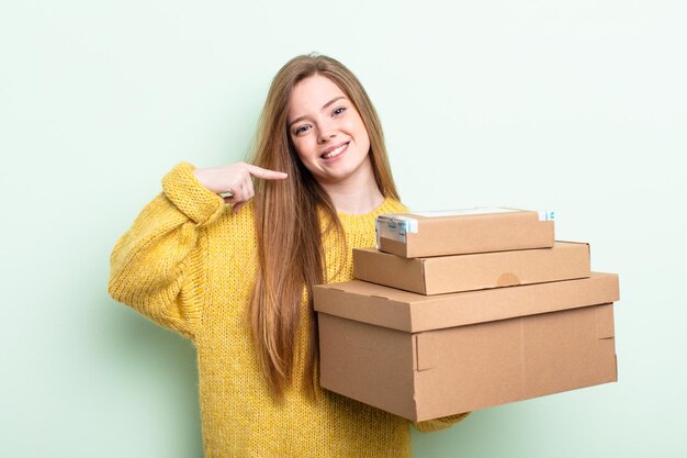 mujer de cabello rojo sonriendo con confianza apuntando a su propia sonrisa amplia. concepto de cajas de paquetes
