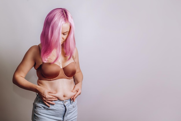 Mujer con cabello rosado aprieta la grasa del vientre en su estómago