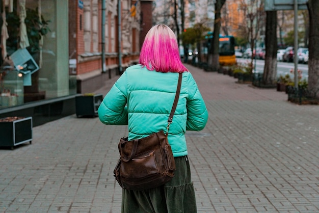 Mujer con cabello rosado y blanco caminando por la calle de la ciudad Fuera de manera positiva Encantador Coloración Freak Ocio Colorido Chaqueta turquesa Atrás Bolso de hombro