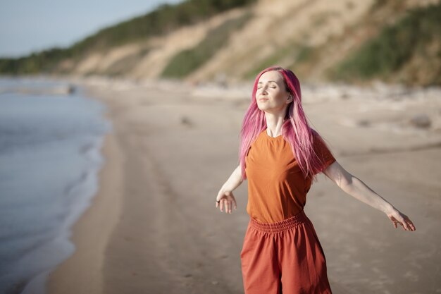 mujer con cabello rosado disfrutando del sol y el viento en la playa