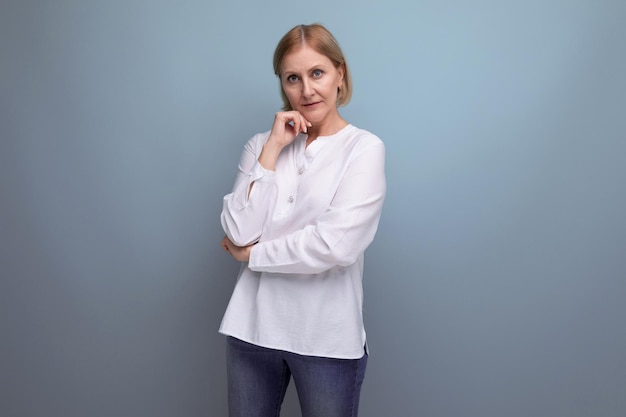 Mujer de cabello rubio de años maduros en una camisa blanca sonriendo sobre un fondo de estudio