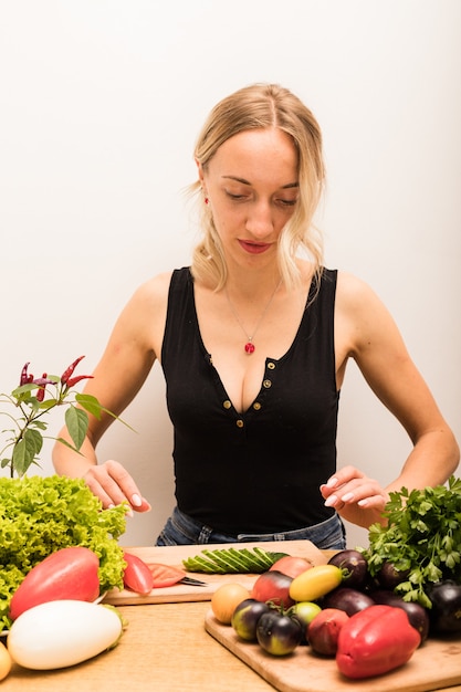 Mujer con cabello rubio corta verduras en la mesa de la cocina