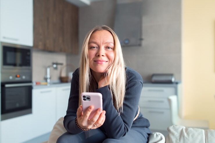 Mujer de cabello rubio con smartphone sentarse en el sofá en casa relajarse tiempo