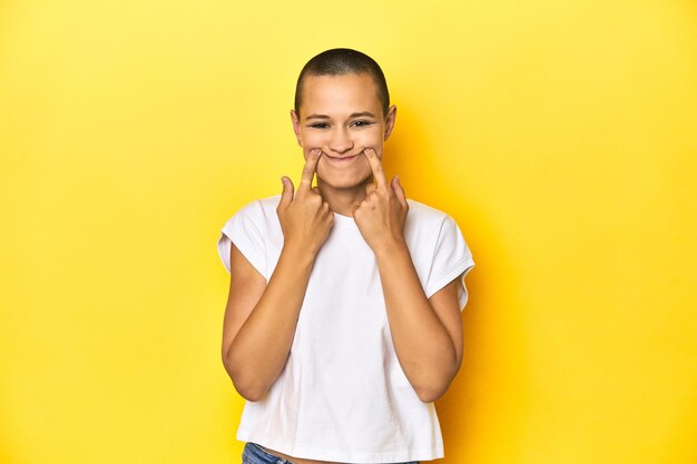 Mujer de cabeza afeitada con camiseta blanca y telón de fondo amarillo dudando entre dos opciones