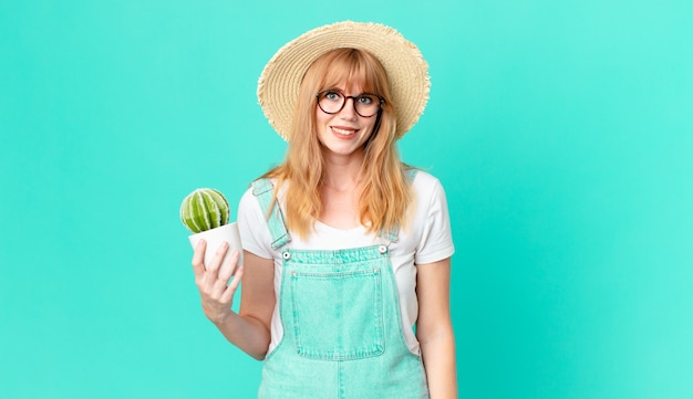 Mujer de cabeza bastante roja que parece feliz y gratamente sorprendida y sosteniendo un cactus en maceta. concepto de granjero