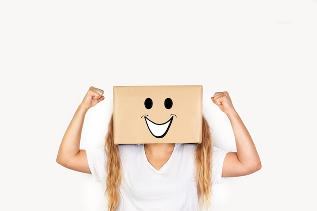 Mujer con la cabeza en una caja y gesto de felicidad dibujado en ella y gesto de brazos de celebración