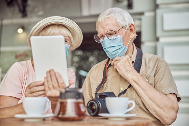 Mujer de cabeza gris sosteniendo su tablet PC delante de un hombre con una mascarilla