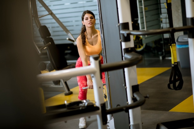 Mujer con cable de barra recta para levantar pesas para ejercitar bíceps en el gimnasio