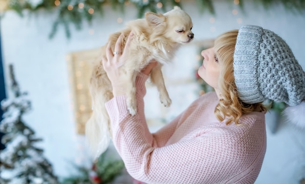 Una mujer con un cachorro de raza pequeña en sus brazos en una foto de Navidad en el fondo del paisaje invernal.