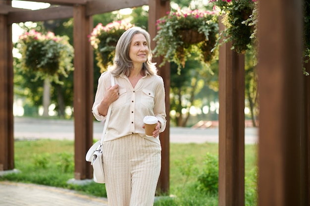 Mujer con café caminando en el parque verde