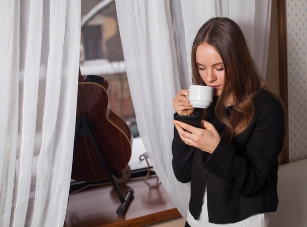 Mujer con café de pie detrás de la guitarra y bebiendo