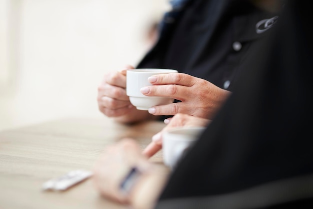 una mujer en un café sostiene una taza blanca de café en sus manos cerradas
