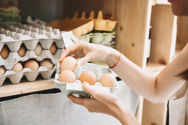 Mujer con caja de cartón de huevos comprando huevos orgánicos bio de la granja local en la tienda de residuos cero