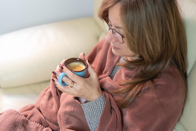 Mujer calentándose las manos con una taza de café caliente mientras disfruta del calor del hogar en pleno invierno