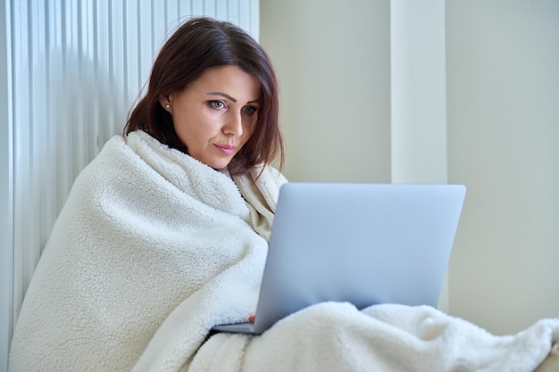 Mujer calentándose con radiador de calefacción de manta usando laptop