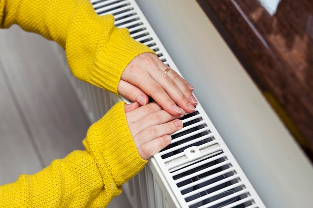 La mujer se calienta las manos en el radiador.