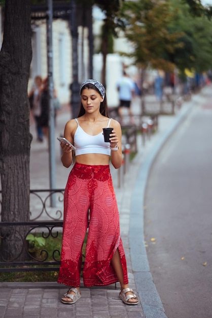 Mujer en la calle tomando café por la mañana y usando un teléfono inteligente