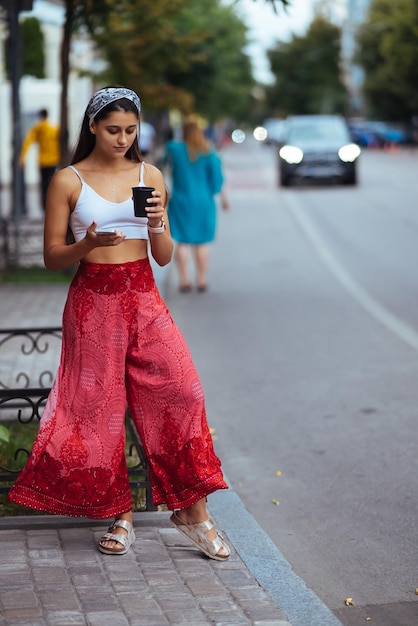 Foto mujer en la calle tomando café por la mañana y usando un teléfono inteligente