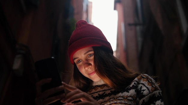 Mujer en un callejón oscuro entre edificios mira su teléfono