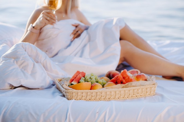 Una mujer en la cama descansa en la orilla del mar con una copa de champán y fruta.