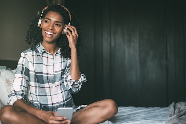 Mujer en la cama escuchando música con auriculares y teléfono inteligente