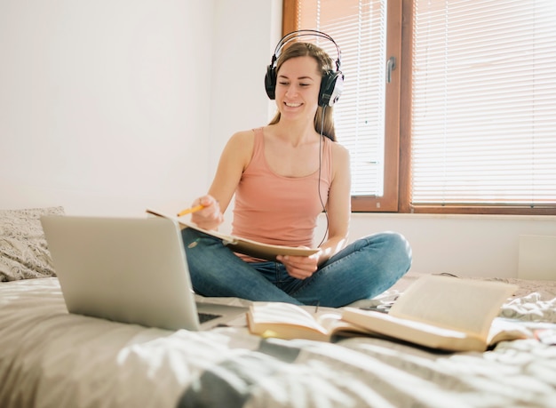 Mujer en la cama con laptop y auriculares participando en una clase en línea