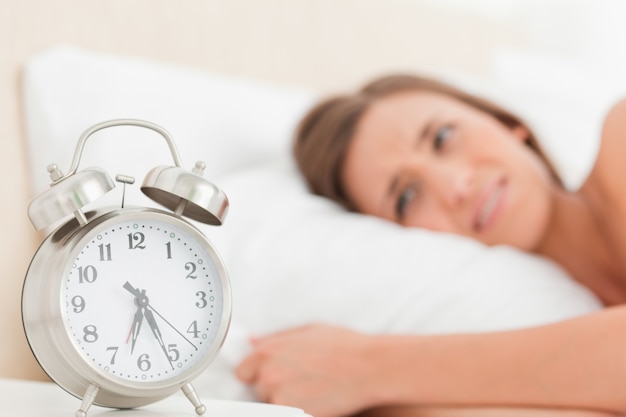 Mujer en la cama con su despertador junto a ella mostrando el tiempo