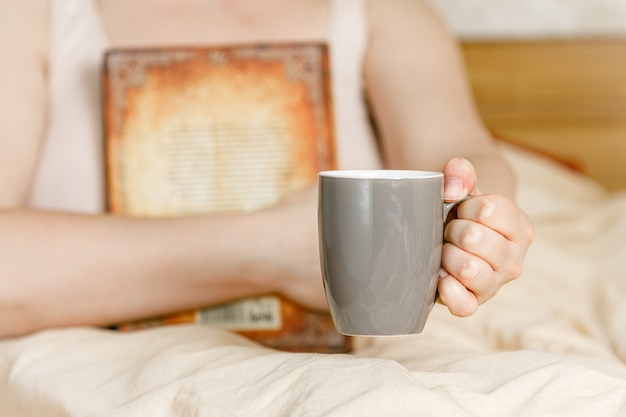 Mujer en la cama con una taza de té y un libro. Mujer adulta leyendo en la cama.