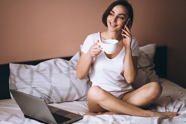 Mujer en la cama con teléfono y café