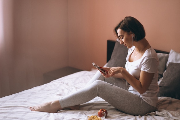 Mujer en la cama con teléfono y comida