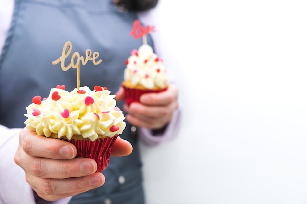 Mujer camarera con dos cupcakes decorados con cobertura de corazones rojos y cartel de madera con letras de AMOR. Concepto de día de San Valentín y día de la madre. Fondo blanco.