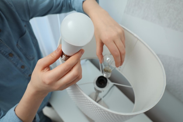 Mujer cambiando bombilla incandescente por una fluorescente en la lámpara en el primer plano de casa Concepto de ahorro de energía