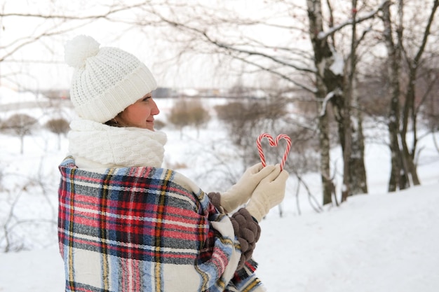 Una mujer camina por el bosque de invierno que sostiene bastones de caramelo en sus manos