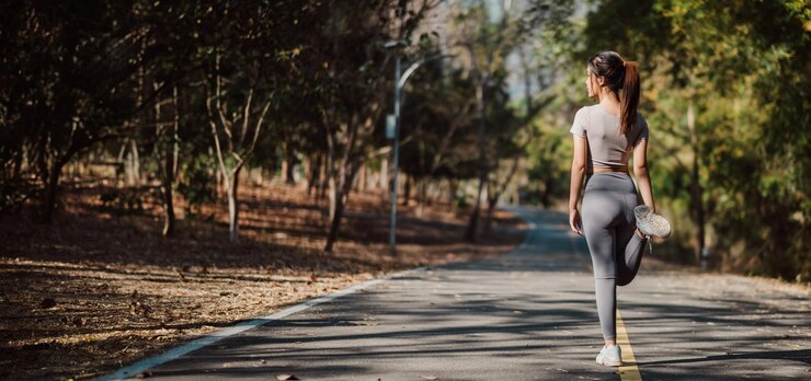 Una mujer camina por la carretera con las piernas abiertas, lleva una camisa gris y pantalones grises.