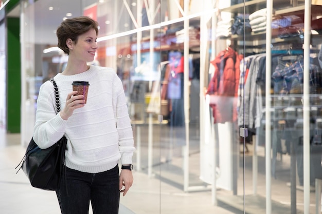 Una mujer camina por el centro comercial con un vaso de café en sus manos mira las ventanas