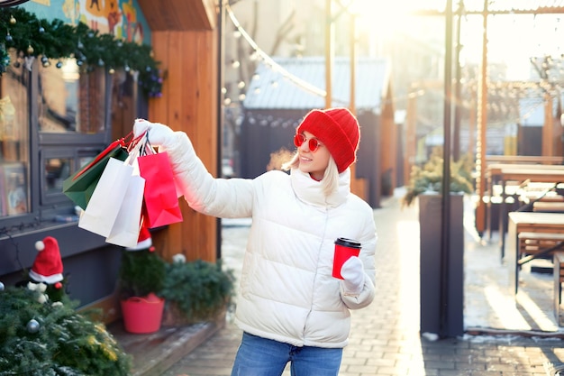 Mujer camina por la ciudad con un montón de bolsas de regalo y bebe café de un vaso desechable