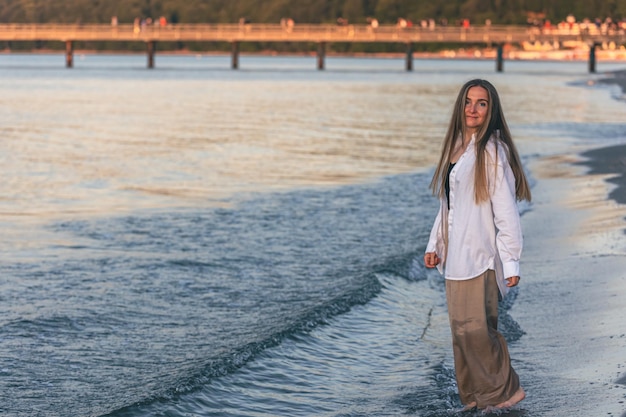 Una mujer camina descalza por el mar en el espacio de la copia al atardecer