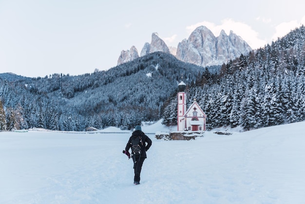 Mujer camina por la nieve a la iglesia en medio de los Alpes con montañas nevadas en el fondo