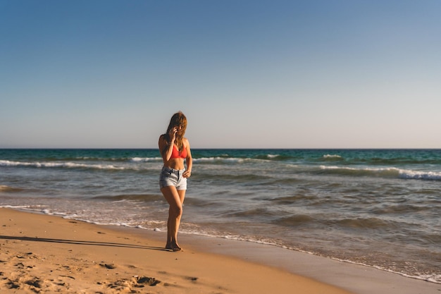 Mujer camina por la orilla del mar mientras habla por su celular