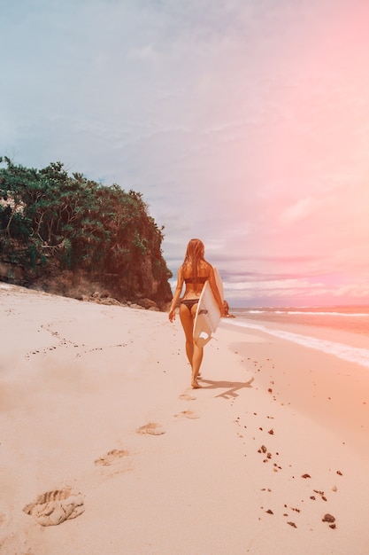 Una mujer camina con una tabla de surf en la playa.