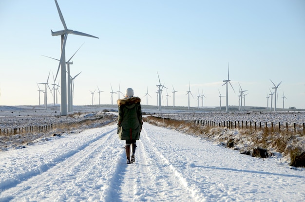 Mujer caminando por una carretera cubierta de nieve contra las turbinas eólicas