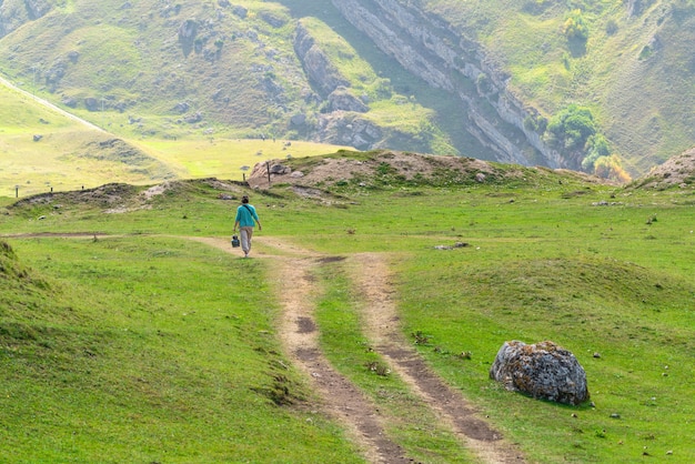 Mujer caminando por una carretera de montaña de tierra con una botella de gas en las manos