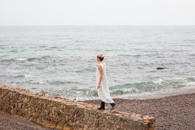 Mujer caminando cerca del mar en otoño Modelo femenino con cabello corto caminando en un día nublado Concepto de tiempo libre de la naturaleza